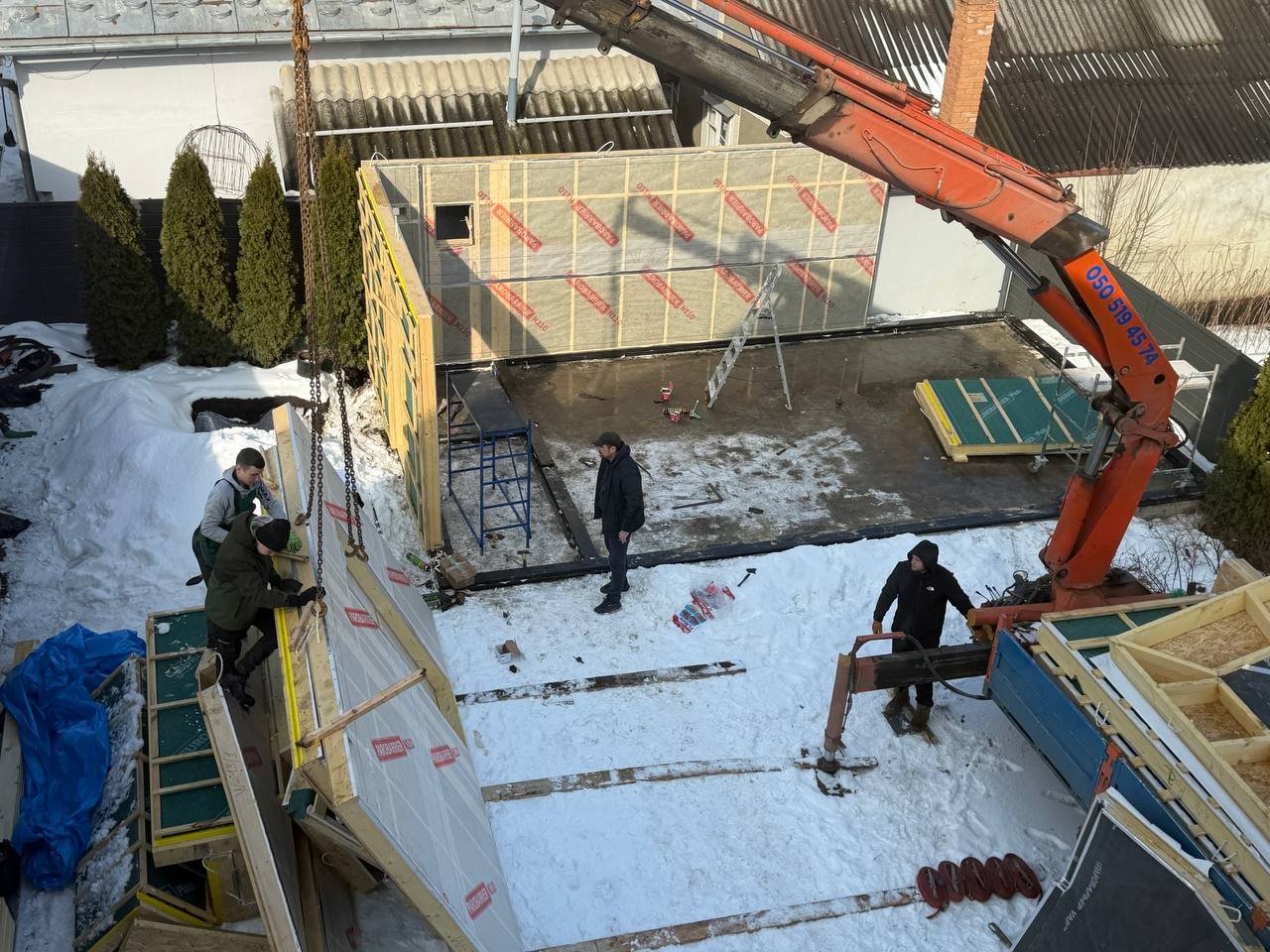 Підйом стінової панелі краном-маніпулятором на фундамент у щільній забудові